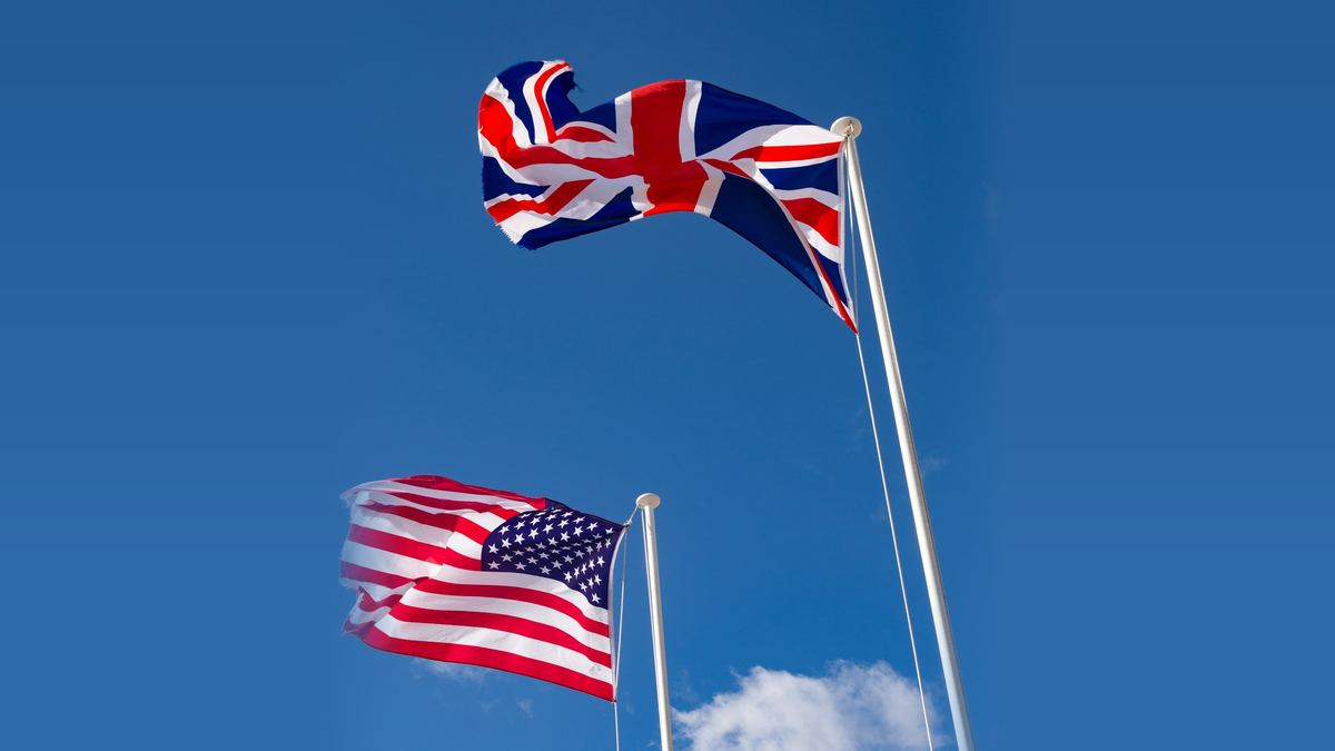 Mavi gökyüzünde iki direkte dalgalanan Amerika ve İngiltere bayrakları
